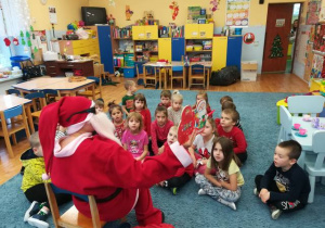 Dzieci siedzą na dywanie Mikołaj czyta świąteczną opowieść.